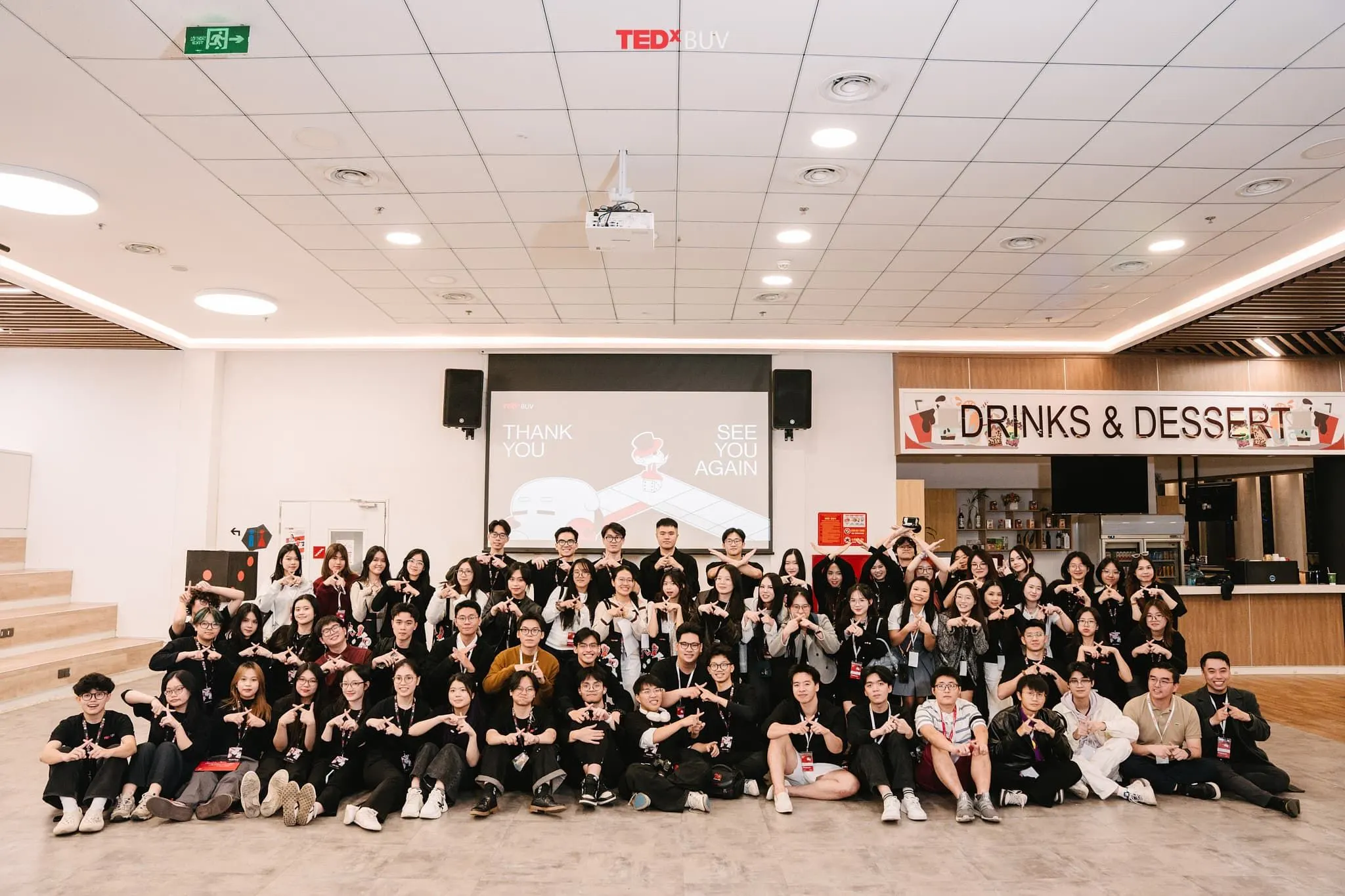 A large group of BUV students pose together in a campus hall beneath a TEDx sign, with a “Drinks & Desserts” counter in the background.