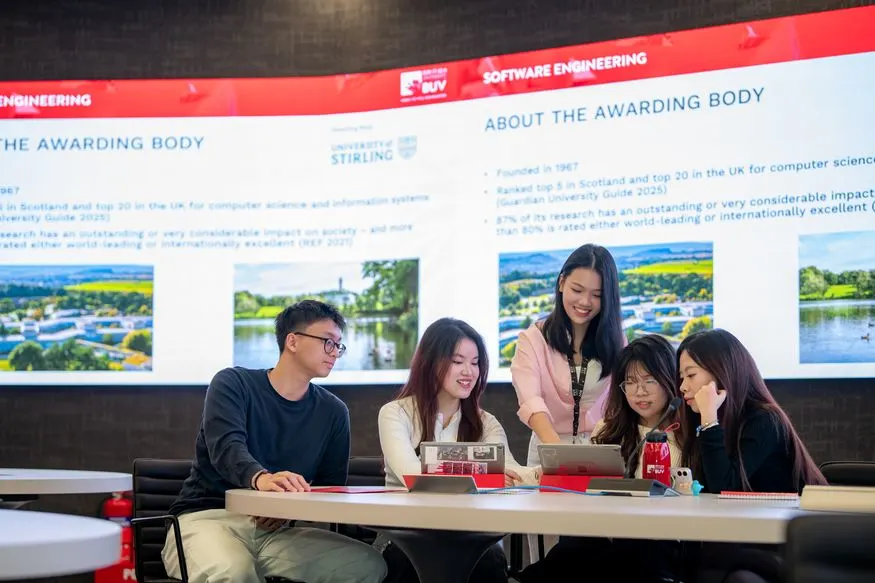 Students collaborate at a table during a presentation, with an “About the Awarding Body” information screen displayed behind them.