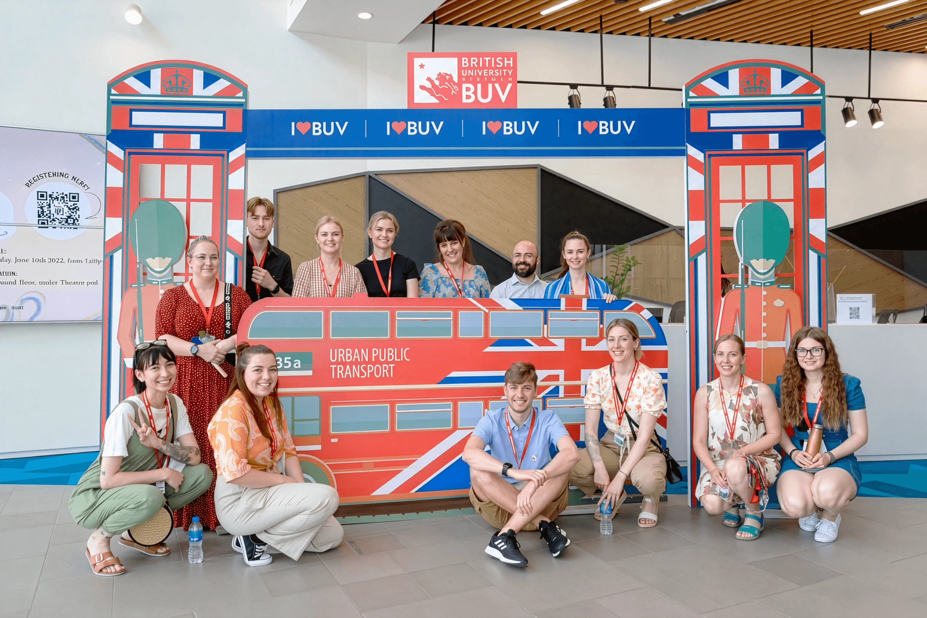 A group of smiling students posing at a British University Vietnam photo booth themed with iconic London elements like a red double-decker bus and phone booths.