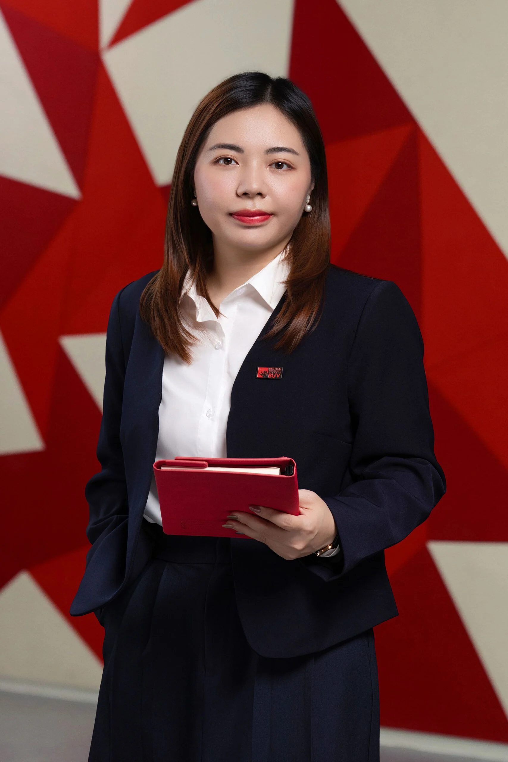 Chân dung nữ giảng viên/sinh viên BUV (Bùi Ngọc Mai) mặc vest xanh, cầm sổ tay và đứng trước phông nền cờ đỏ trắng.