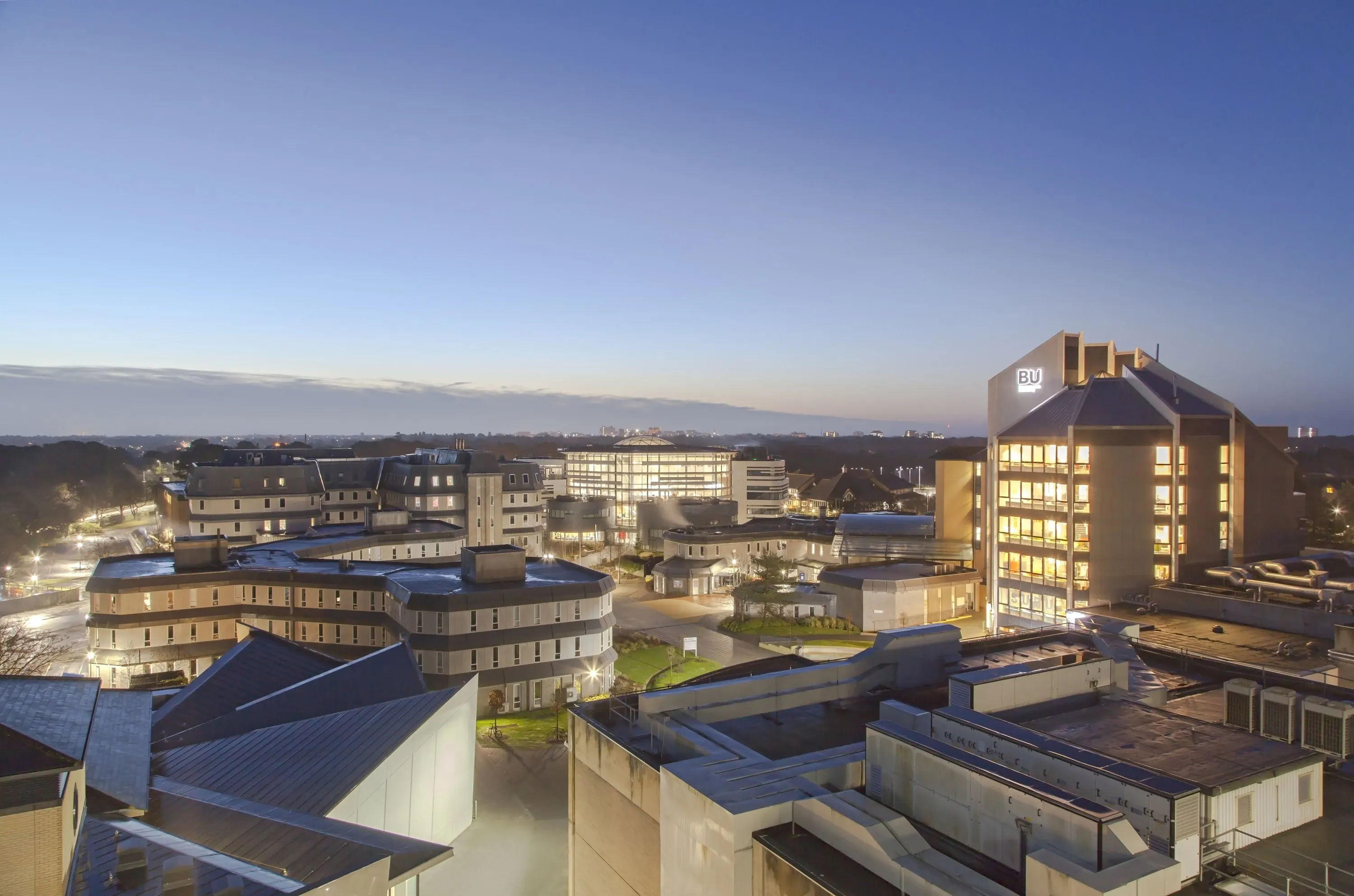 BU campus buildings illuminated at dusk, showcasing modern university facilities and surrounding cityscape.