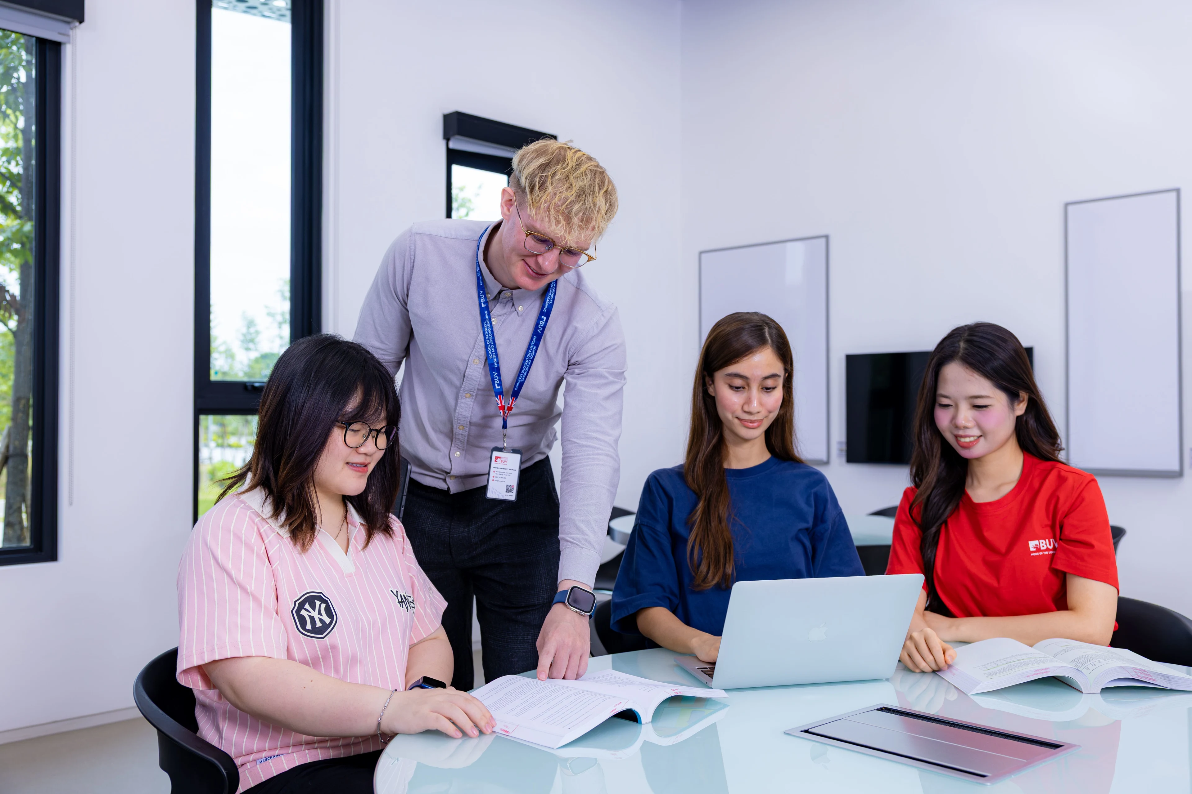 International lecturer guides BUV students using a laptop and textbooks in a modern classroom.