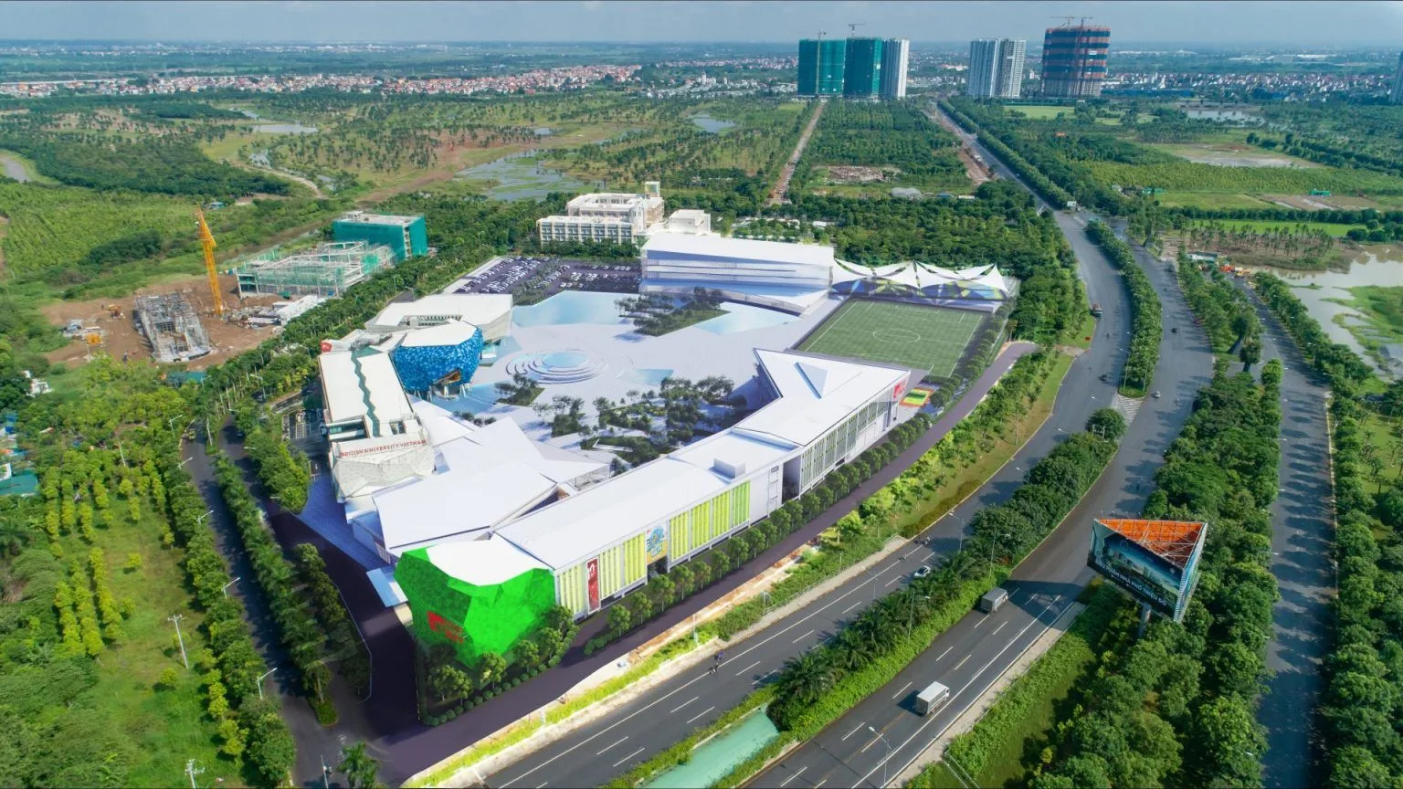 Aerial view of a modern university campus with white buildings, landscaped grounds, surrounding greenery, and roads.