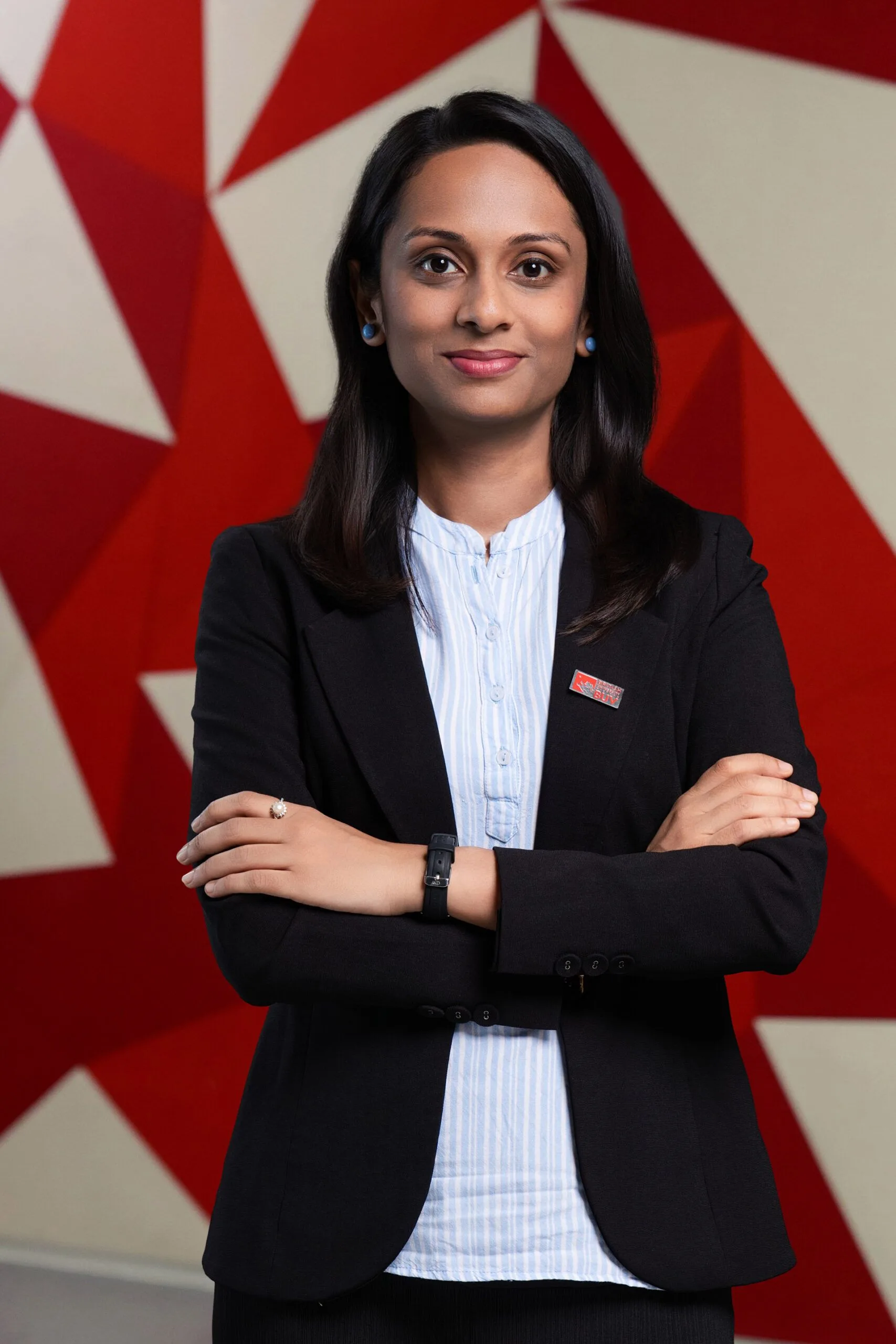 Dr Aiwa Romy, BUV faculty member, standing with folded arms against a red geometric background