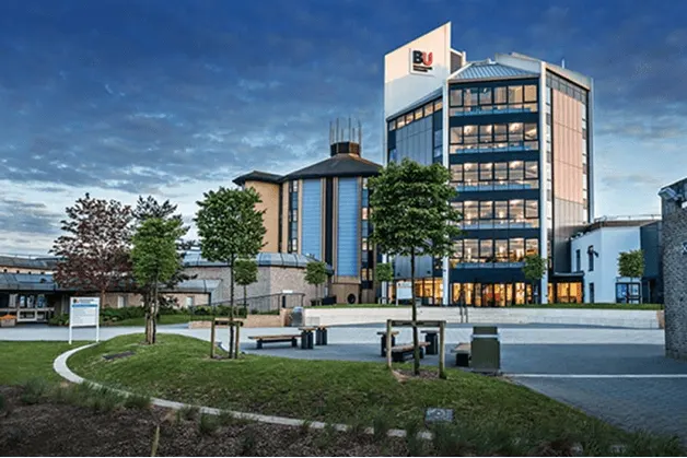 British University Vietnam campus with modern multi-storey academic buildings, landscaped gardens, and walkways under a cloudy blue sky.