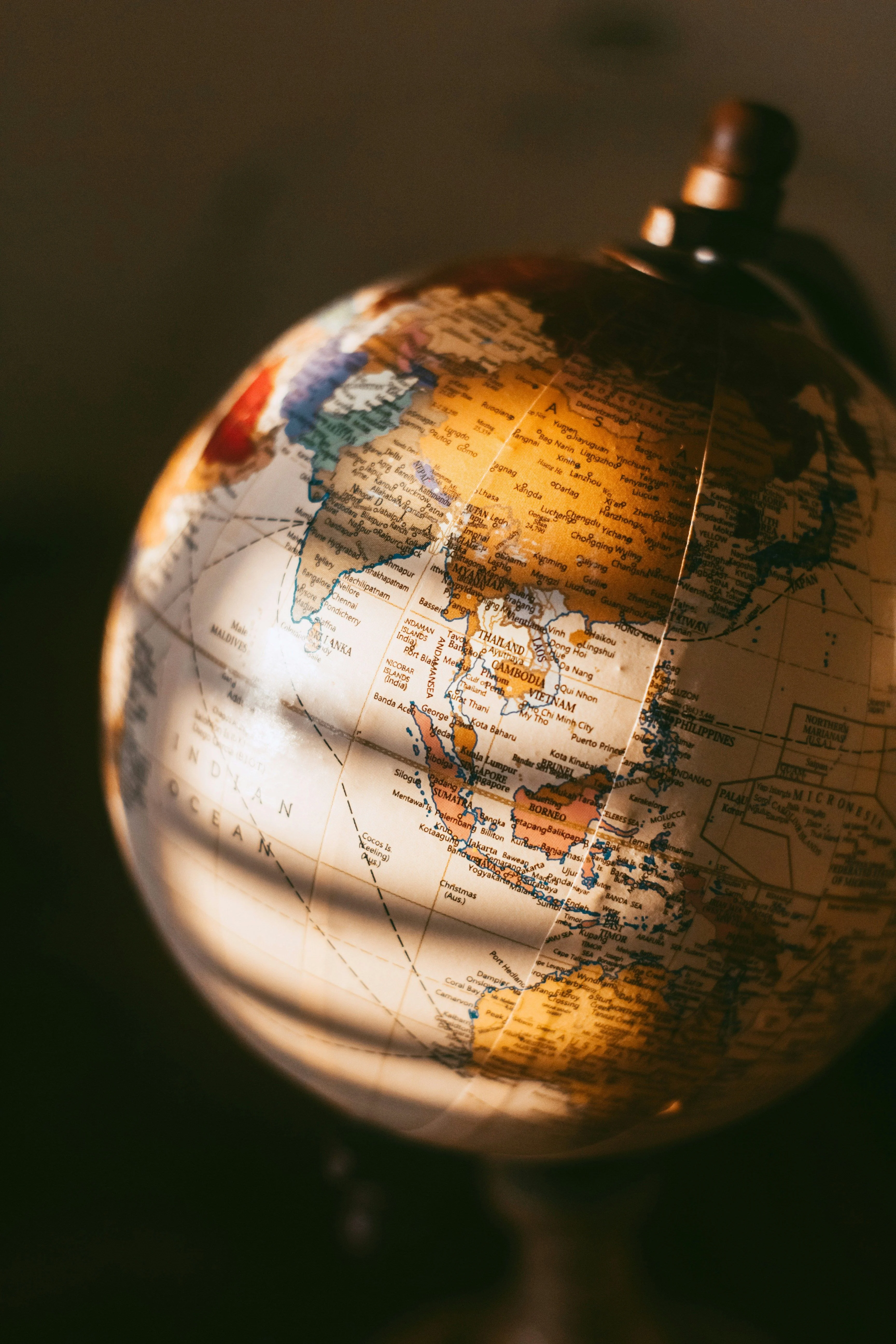 Close-up shot of a vintage desk globe illuminated by warm sunlight, focusing on Southeast Asia and the Indian Ocean.