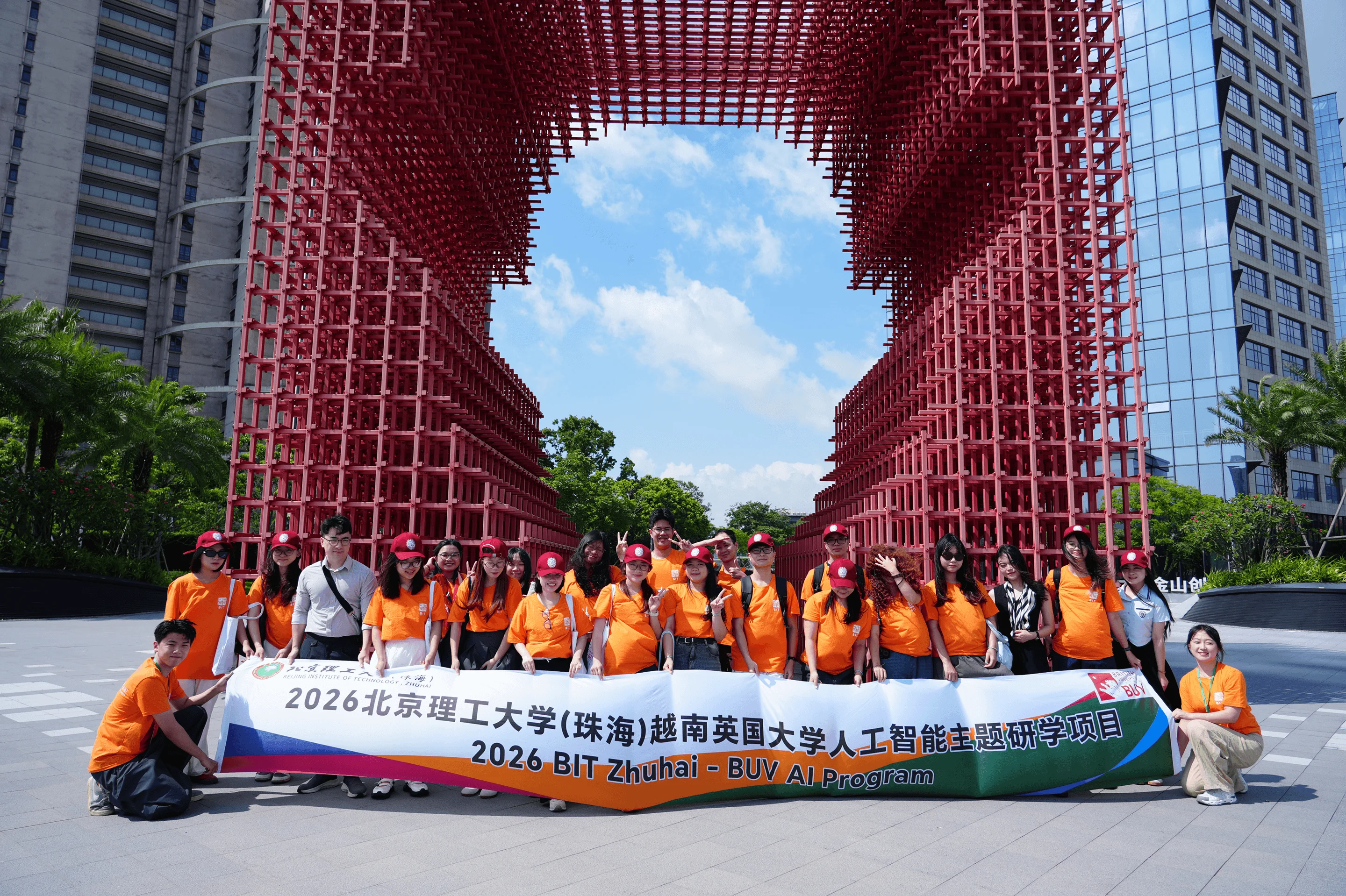 A group of students in orange shirts posing with a banner for the 2026 BIT Zhuhai - BUV AI Program in front of a large, red geometric arch structure.