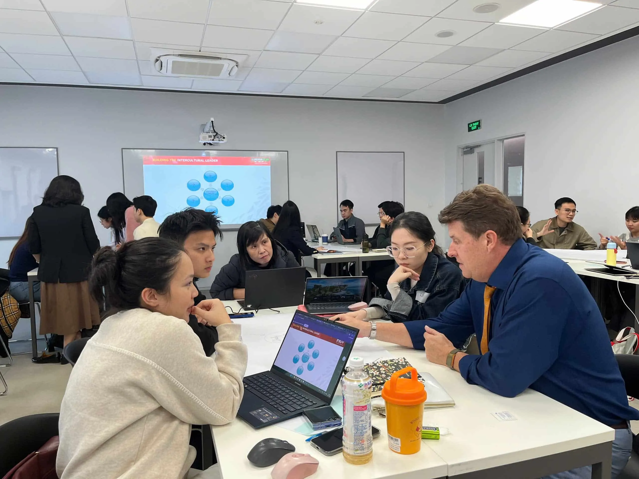 Students and a lecturer collaborate around laptops during an interactive classroom workshop.