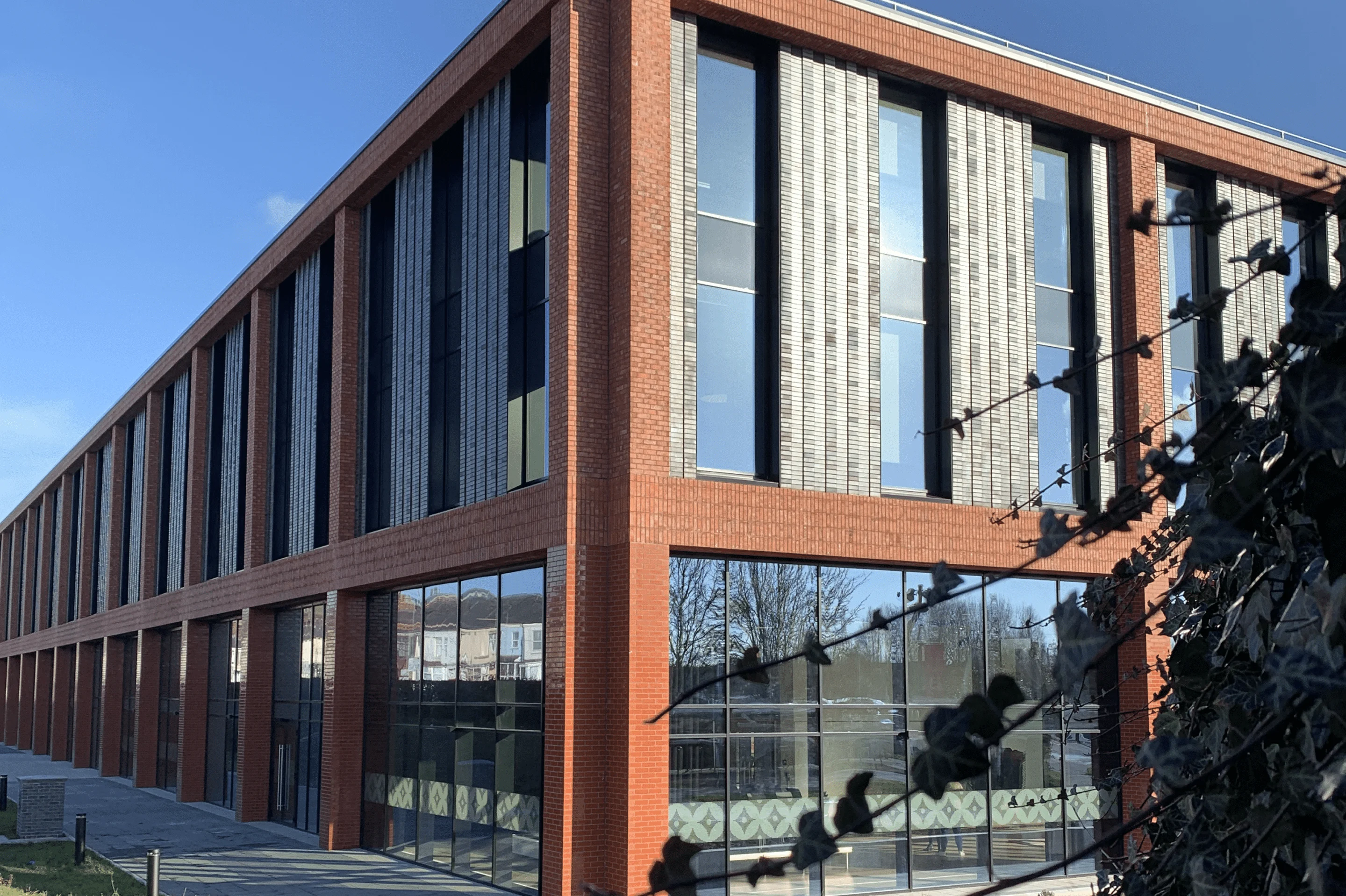 A modern, red-brick multi-storey building at Staffordshire University, featuring large glass windows and vertical panels under a clear blue sky.