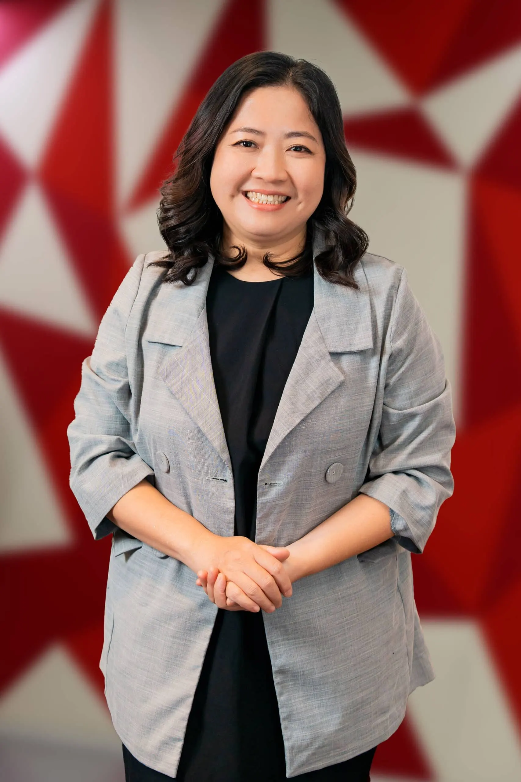 A smiling woman, Dr. Hoang Phuong, wearing a light gray blazer over a black top, posed in front of a red geometric background.