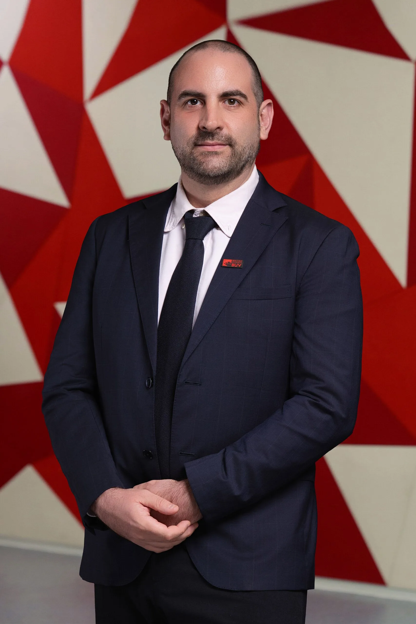 Chân dung Julien Psonmas mặc vest, đeo huy hiệu British University Vietnam trước nền đỏ trắng.