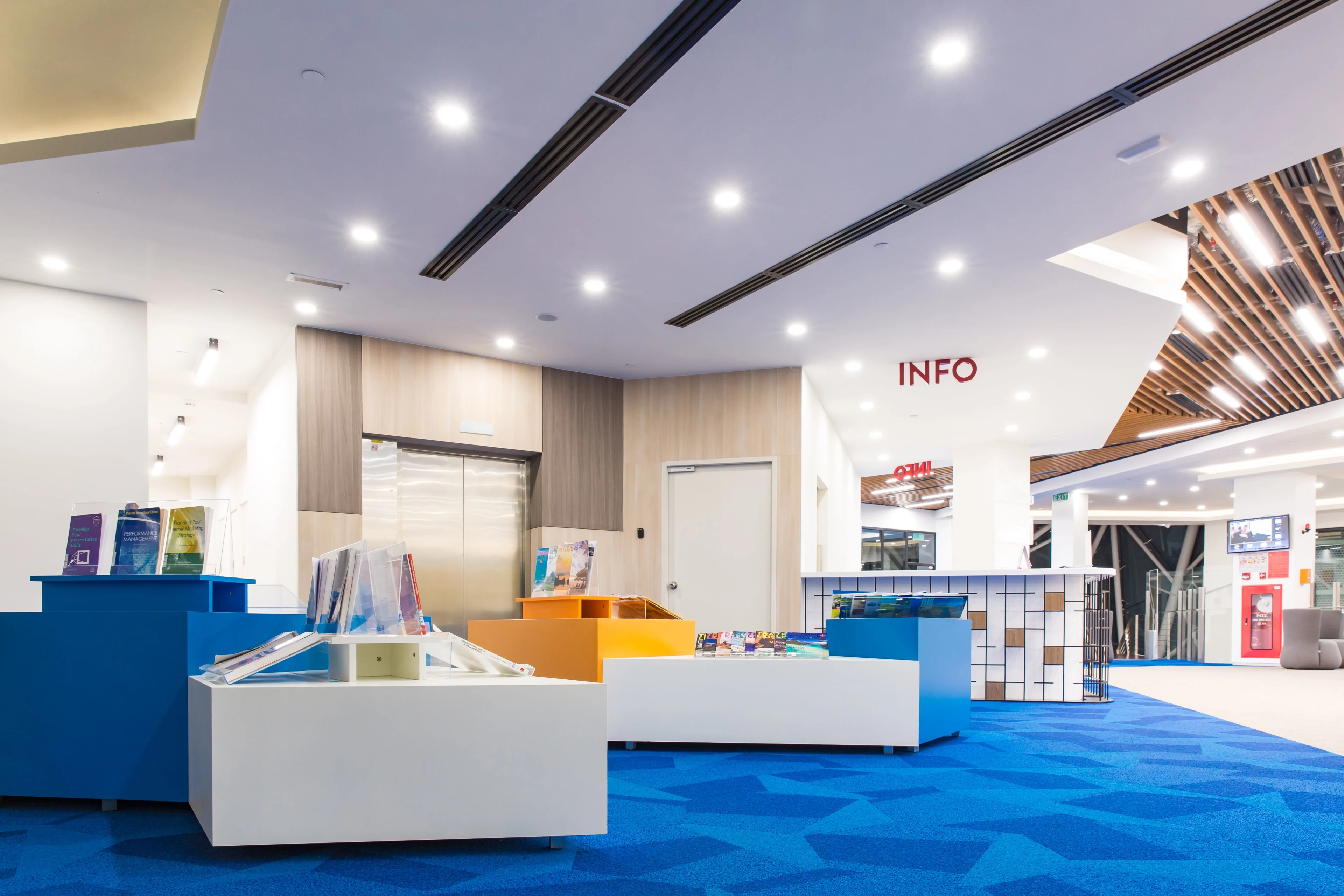 BUV campus information area with colorful reception desks, university brochures, elevator and blue carpet.