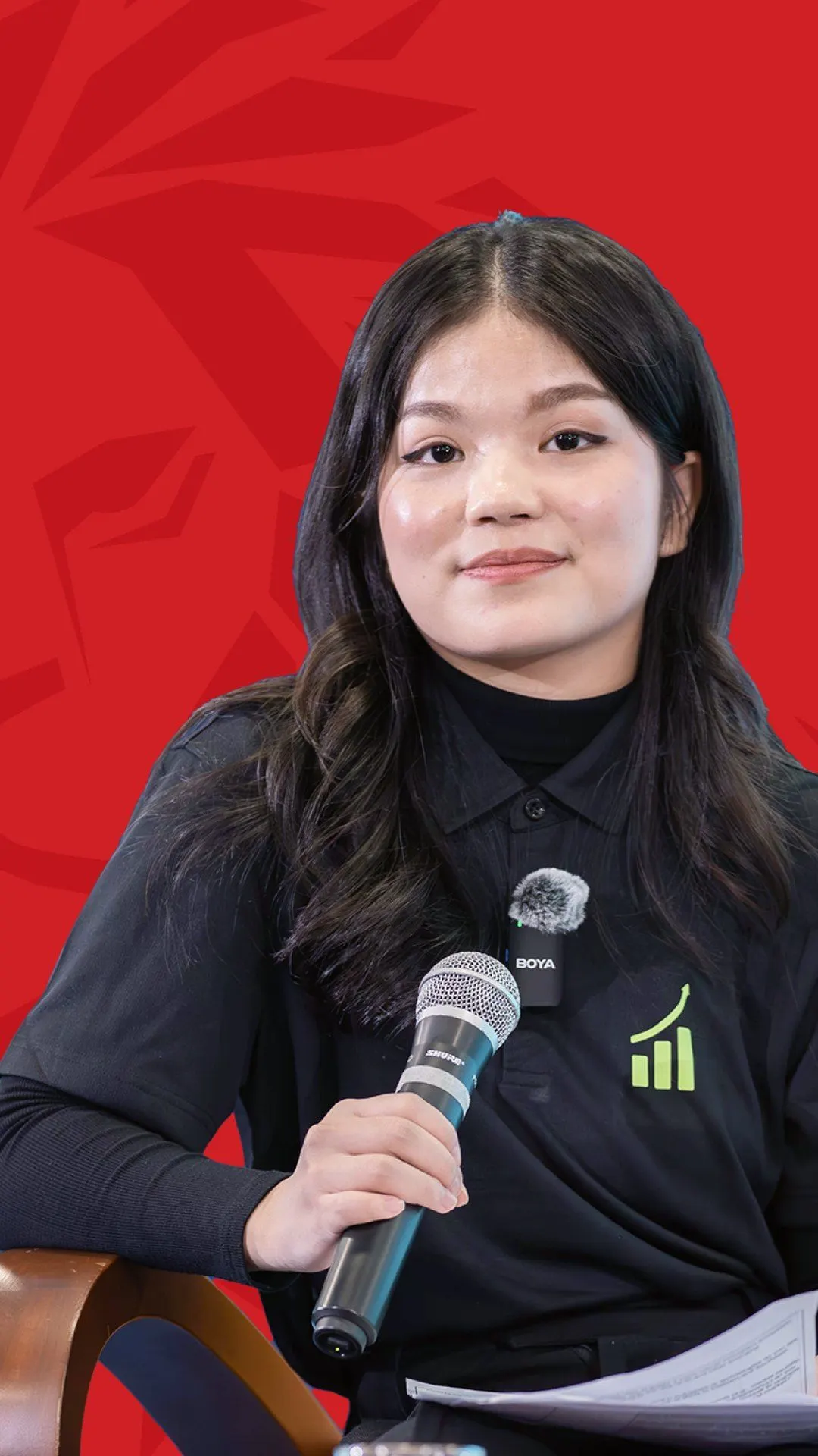 BUV alumna Minh Yen speaks into a microphone during an interview against a red Lionhearted backdrop.