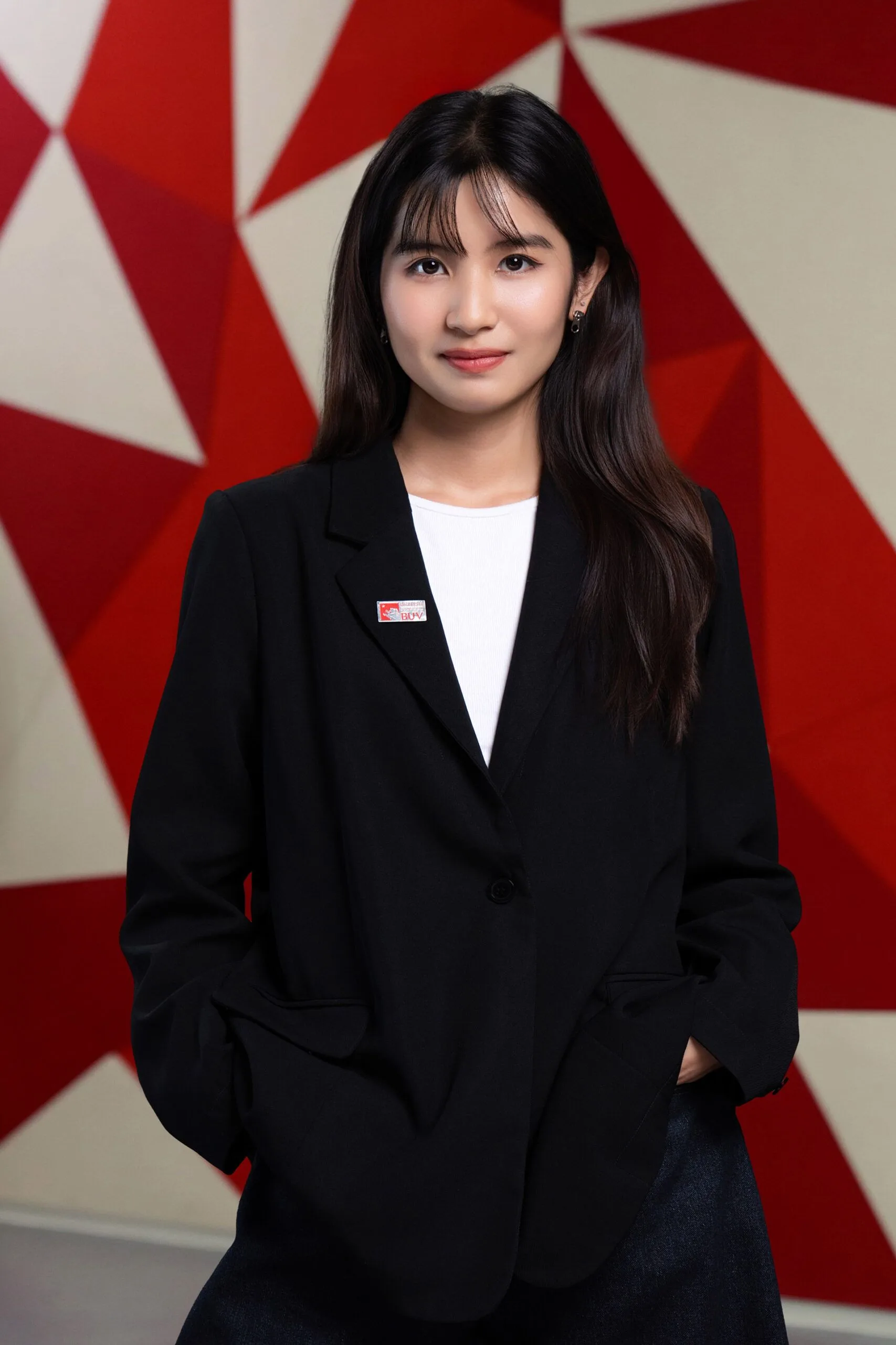 Portrait of Pham Thuy Duong wearing a black blazer and standing in front of a red geometric backdrop.