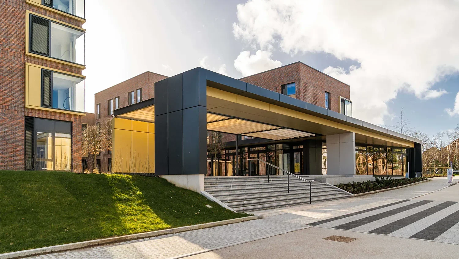An exterior shot shows a modern building entrance with wide stairs and a yellow overhang.