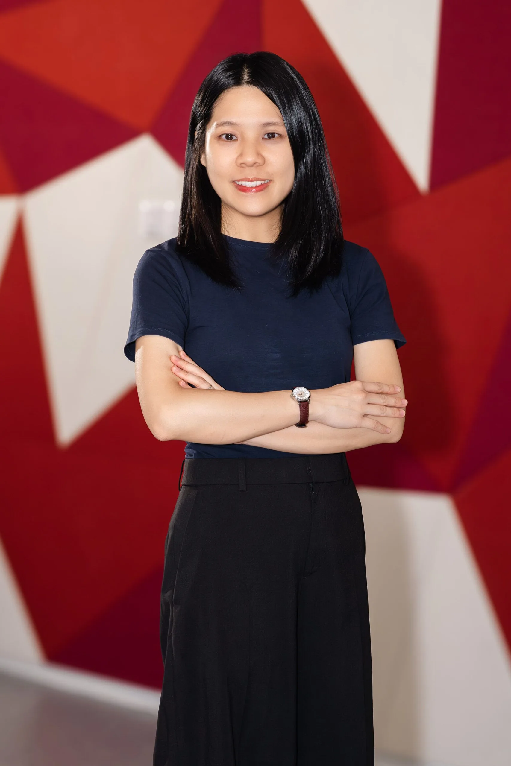 Portrait of Daphne Lau standing with arms crossed in front of a red and white backdrop.