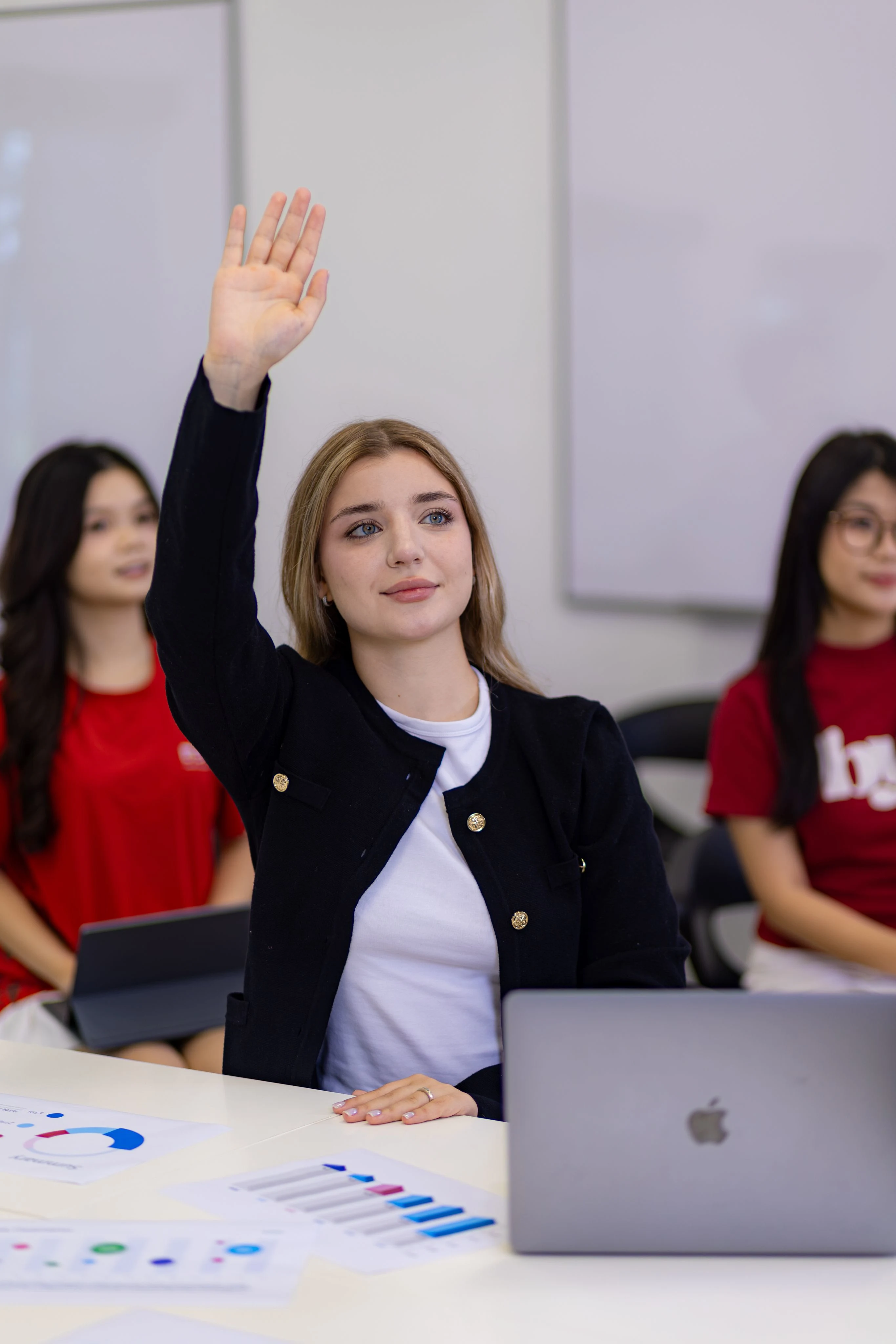 International student at BUV raises her hand during an interactive university class with a laptop and charts