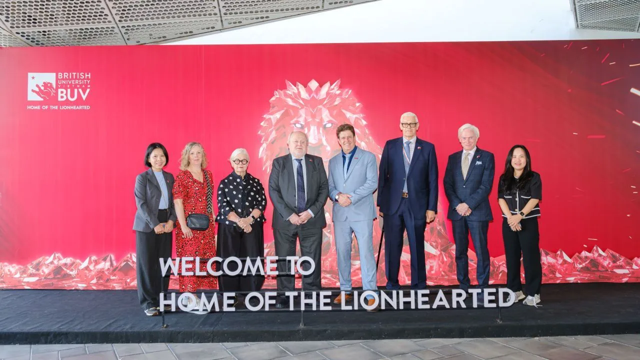 Representatives pose at British University Vietnam (BUV) beneath a “Welcome to Home of the Lionhearted” sign.