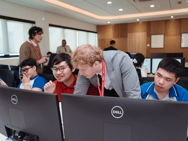 University students collaborate at desktop computers while an instructor leans in to provide guidance in a modern classroom.