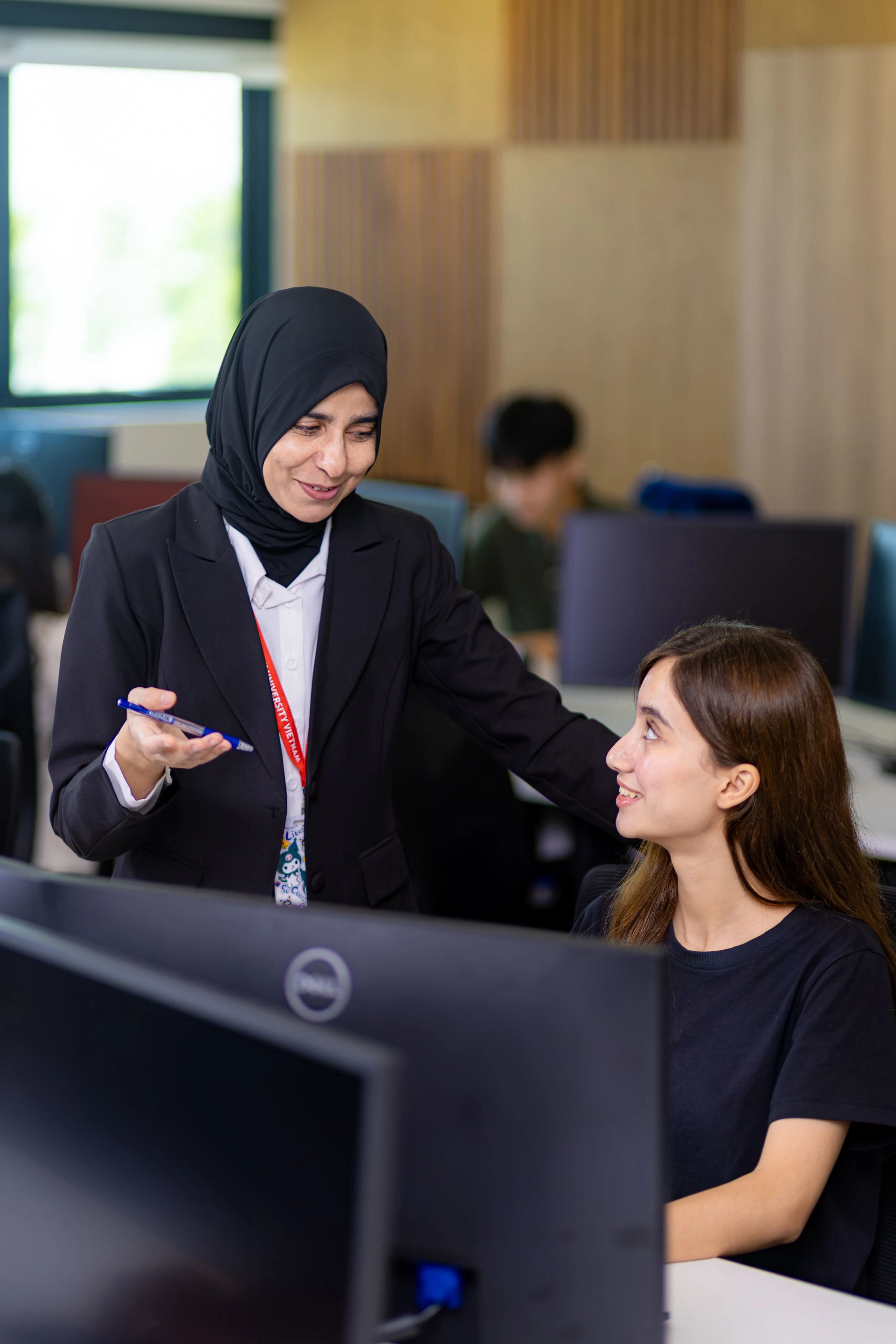 BUV lecturer guides a student at a desktop computer in a modern university lab