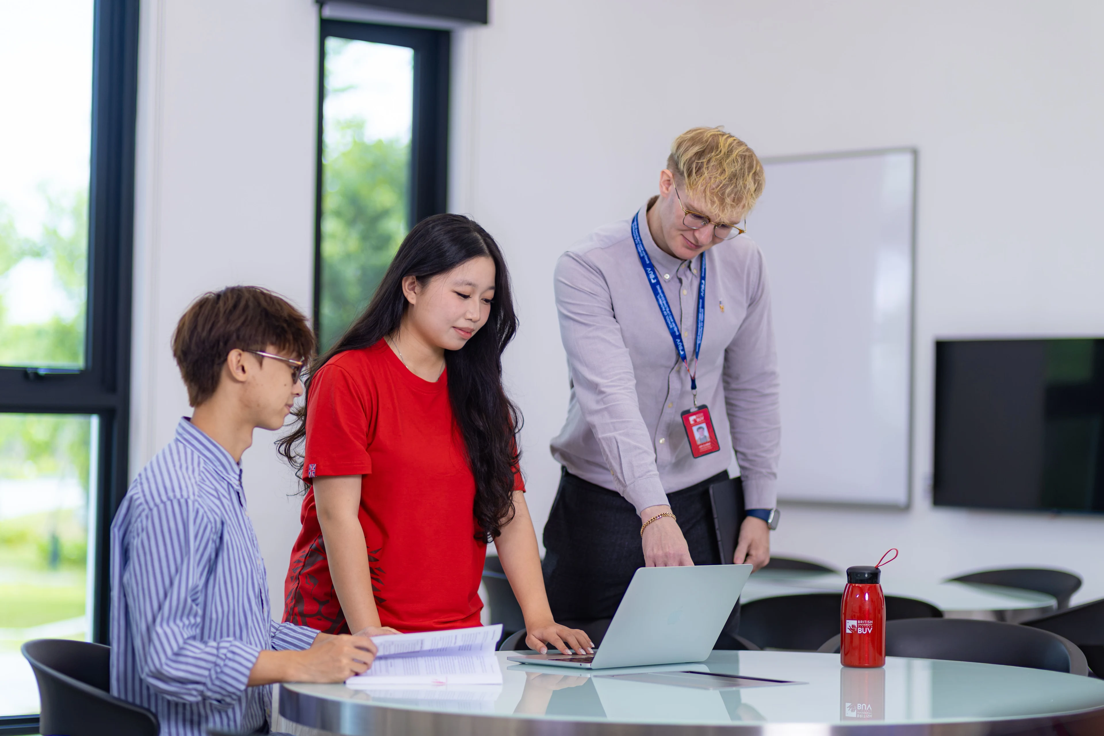 BUV lecturer guides two students using a laptop in a modern classroom at British University Vietnam.