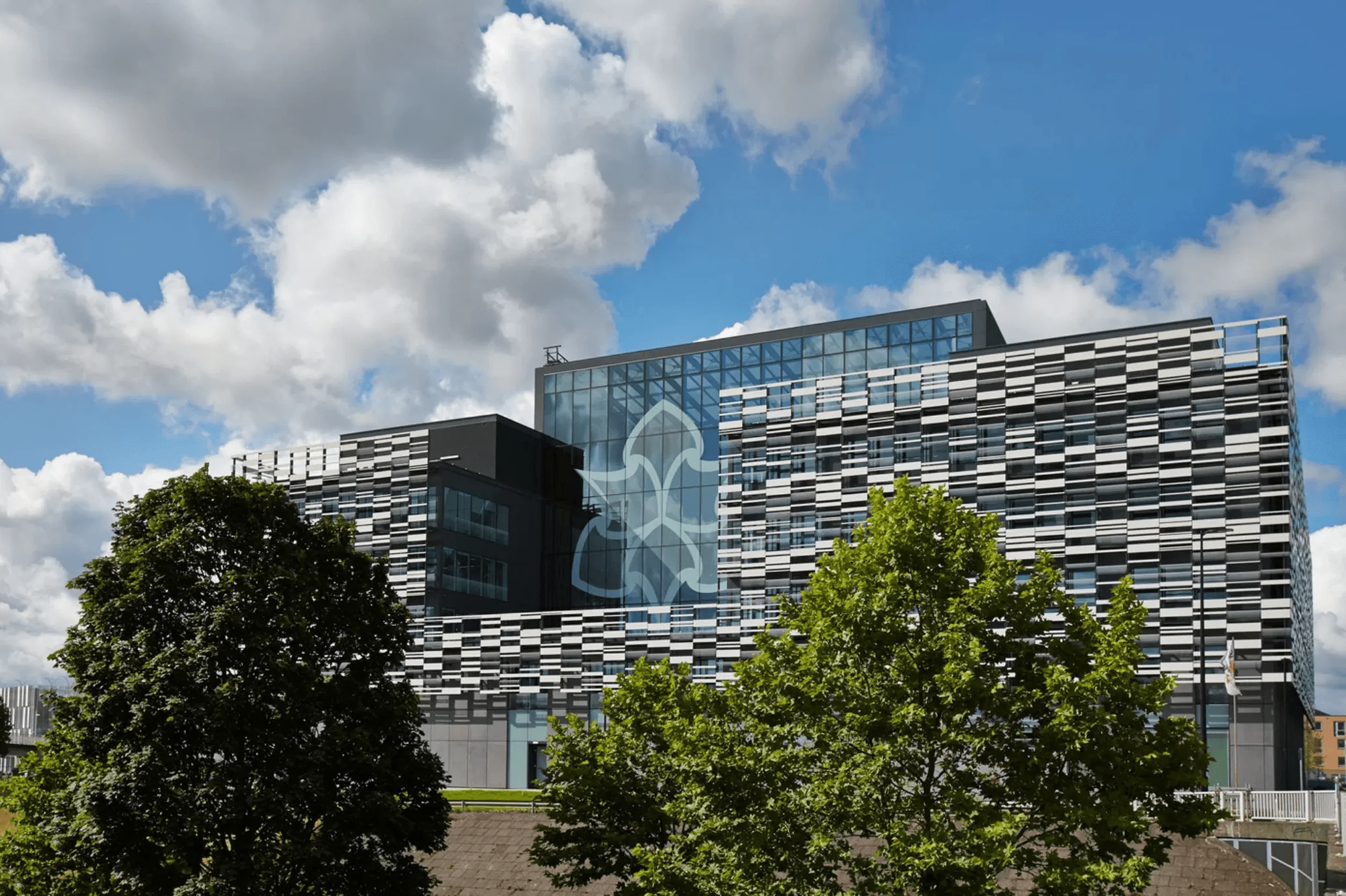 Manchester Metropolitan University’s modern campus building beneath a blue, cloud-filled sky.