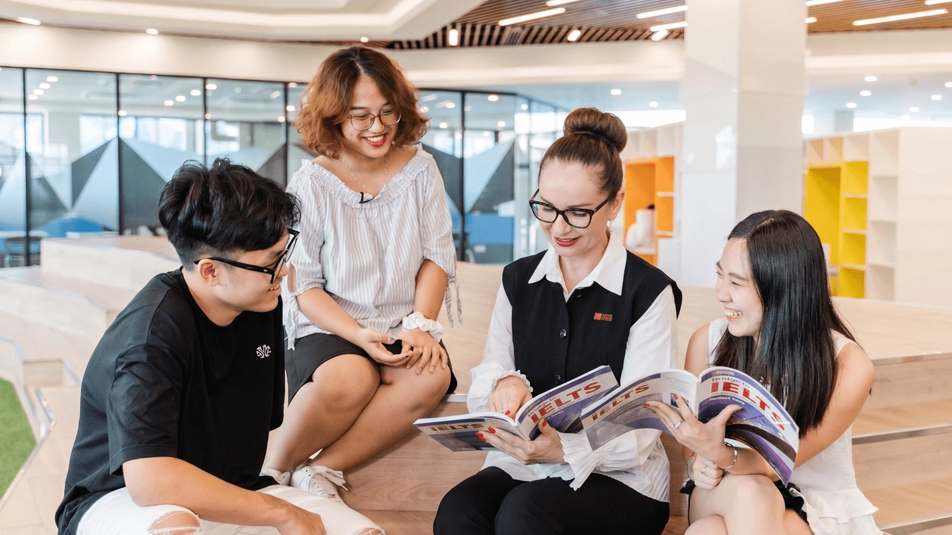 BUV students and staff reading IELTS materials together in a modern British University Vietnam campus lounge.