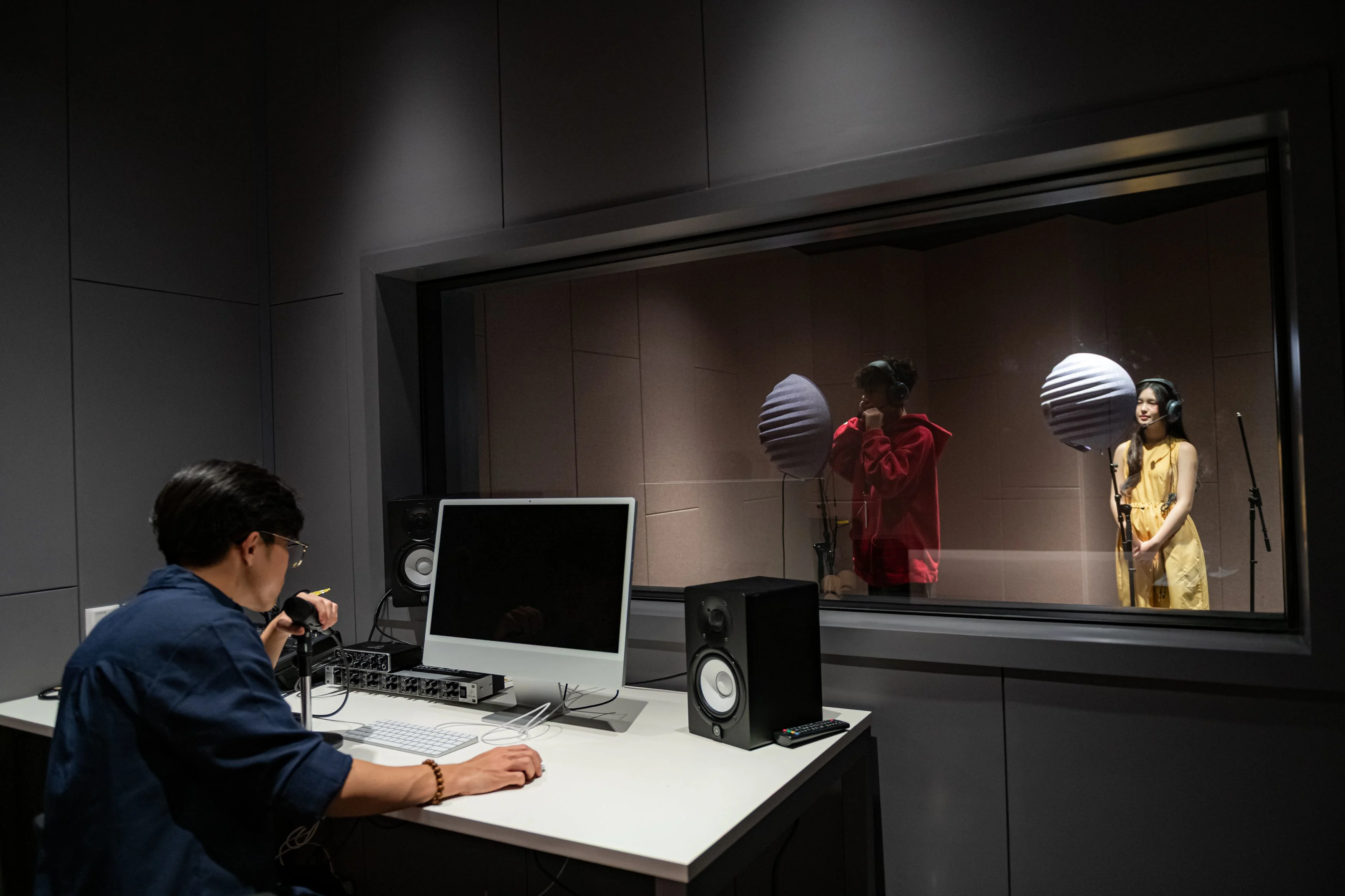 BUV music production studio with student engineer recording two singers behind a soundproof window