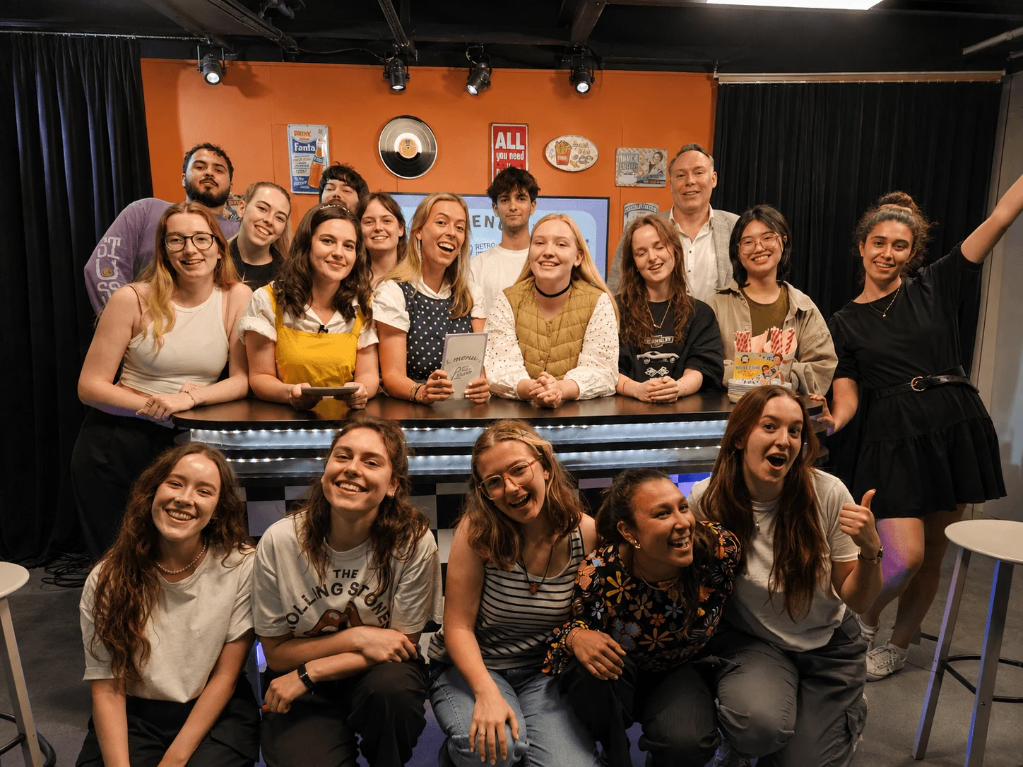 A diverse group of exchange students smile and pose together in a lively indoor venue.