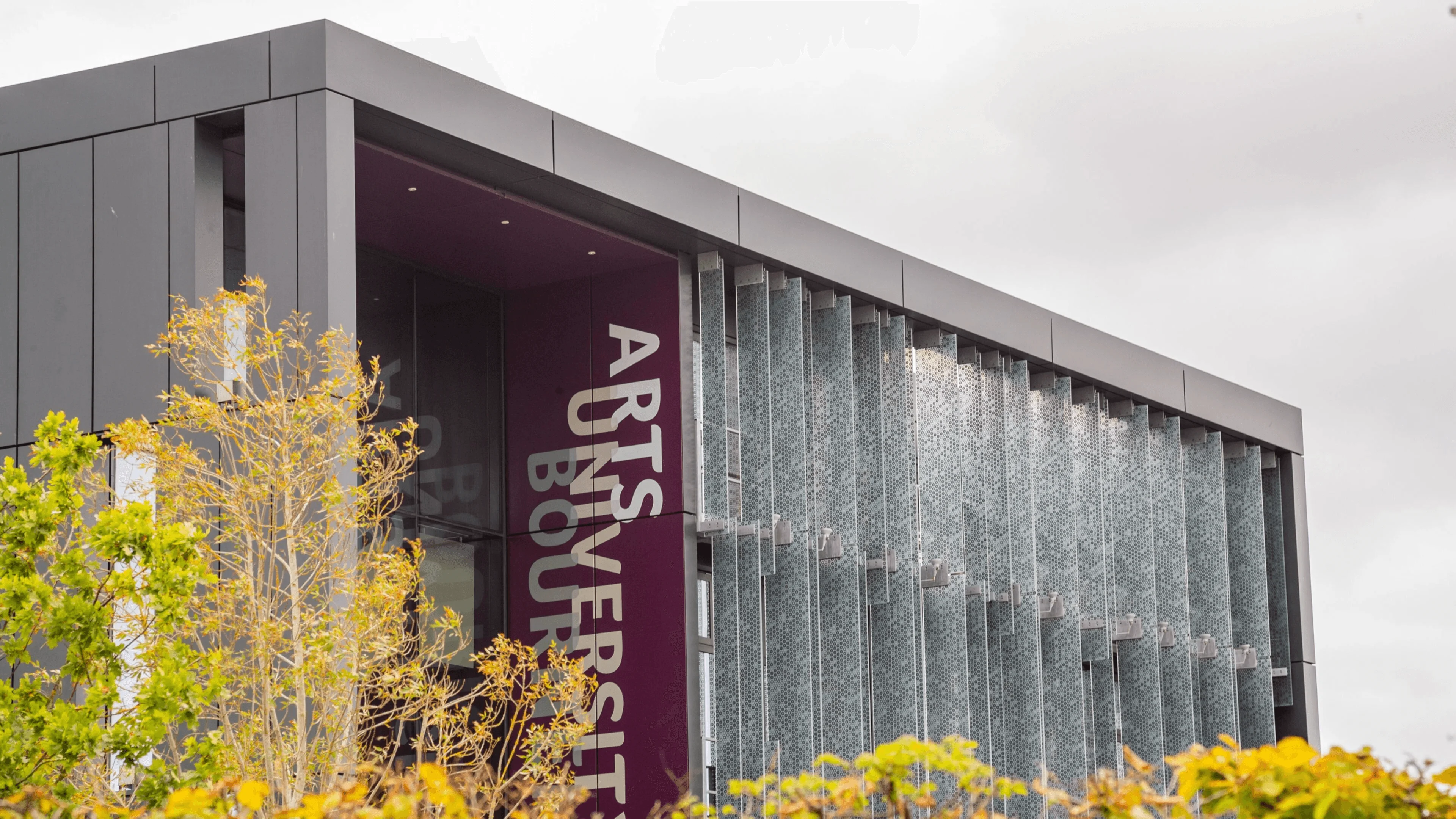 Modern exterior of Arts University Bournemouth, featuring a glass façade and vertical university sign.