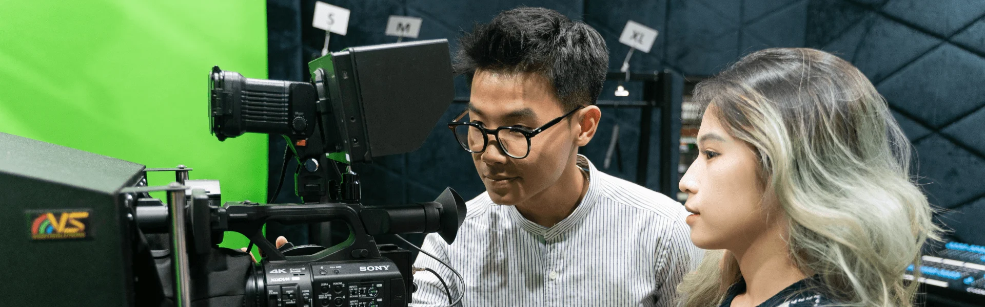 Two BUV students operating professional video equipment in a green-screen studio.