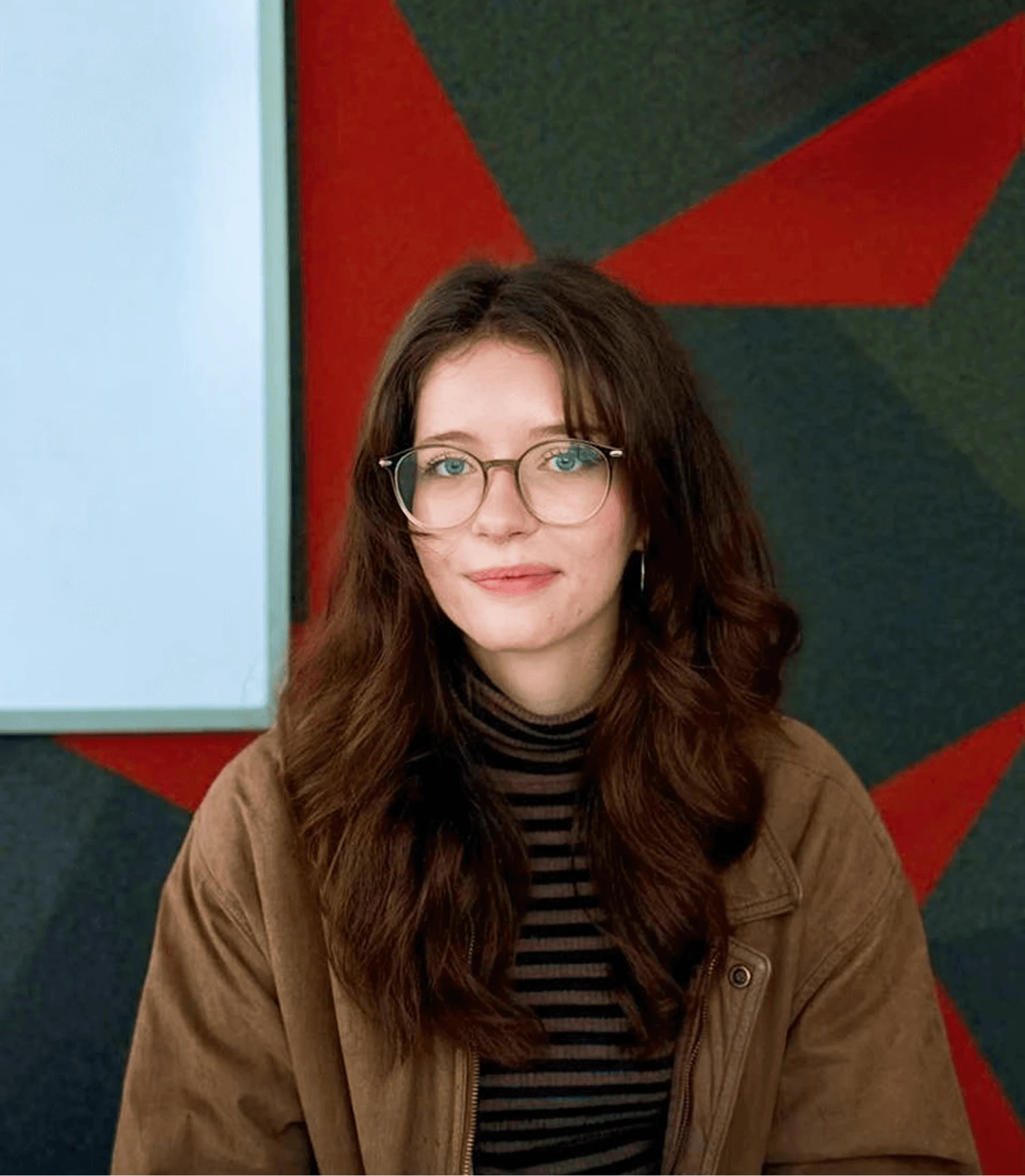 Young woman wearing glasses and a brown jacket against a geometric red and black backdrop