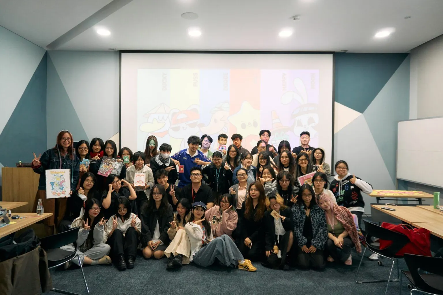A large group of students and instructors pose for a photo in a classroom in front of a projection screen.