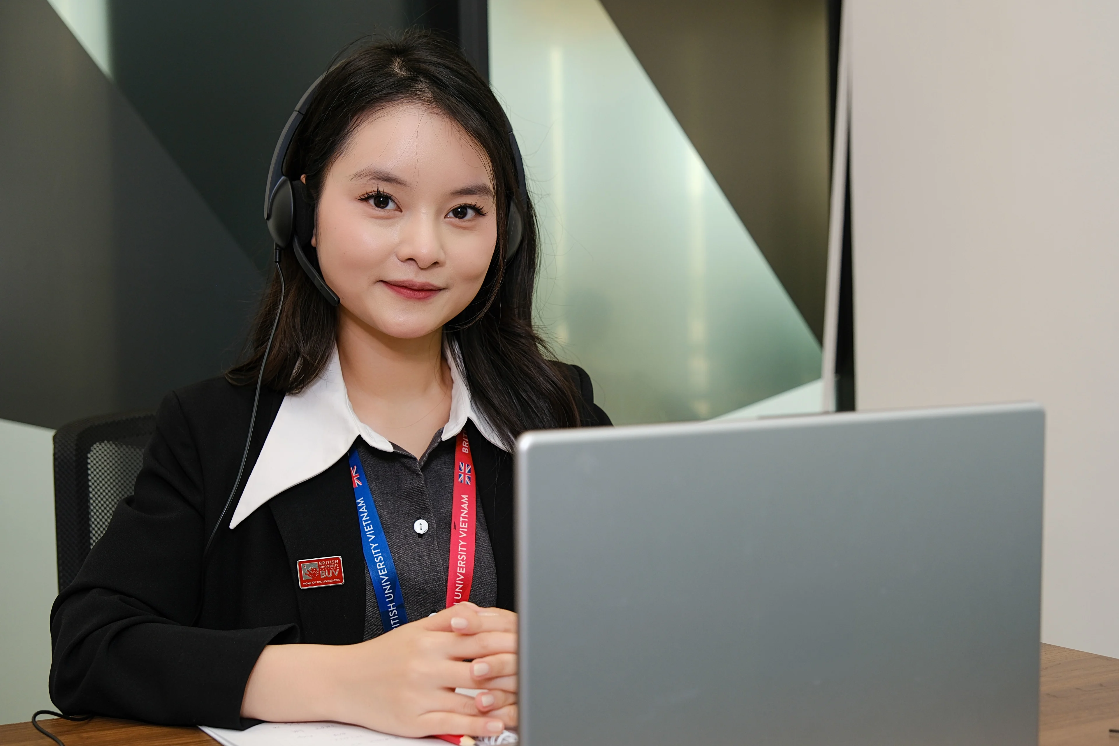 British University Vietnam staff member wearing a headset provides online student support via laptop.